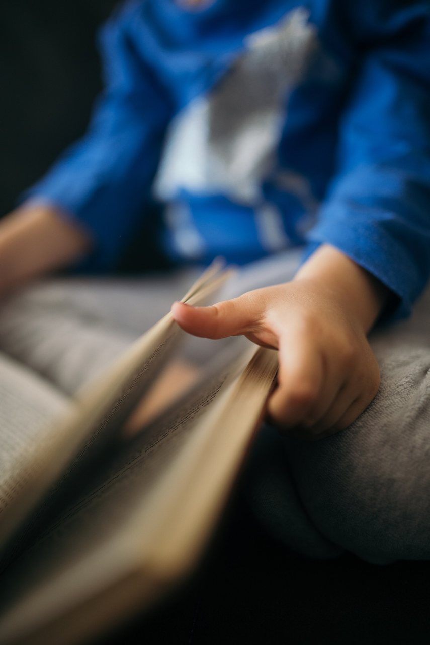 Ребенок читает книгу, сидя на мягкой поверхности.